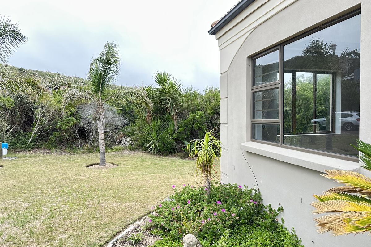 A view of the rear garden area featuring a well-maintained lawn, established landscaping, and the side elevation of the house with aluminum-framed windows.
