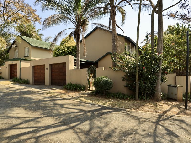 Front elevation of a townhouse featuring a double garage, pedestrian gate, and established garden surroundings in a quiet residential setting.