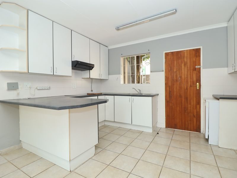 A functional kitchen featuring white cabinetry, laminate countertops, tiled flooring, and a rear timber door, offering a clean canvas for modern updates.