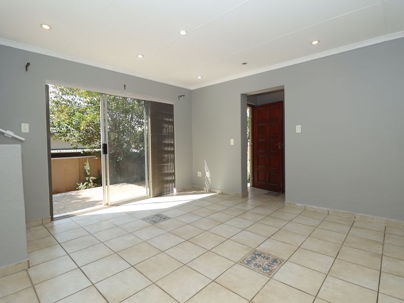 An empty, open-plan living area featuring tiled floors, recessed lighting, and direct access to an outdoor patio through a sliding glass door.