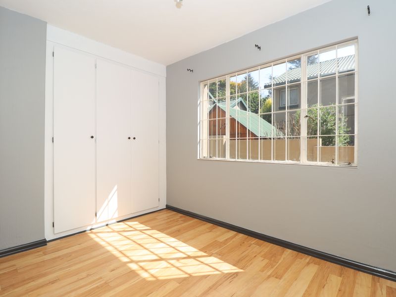 A bright, empty bedroom featuring polished timber flooring, built-in cupboards, and a large grid-pattern window allowing for ample natural light.