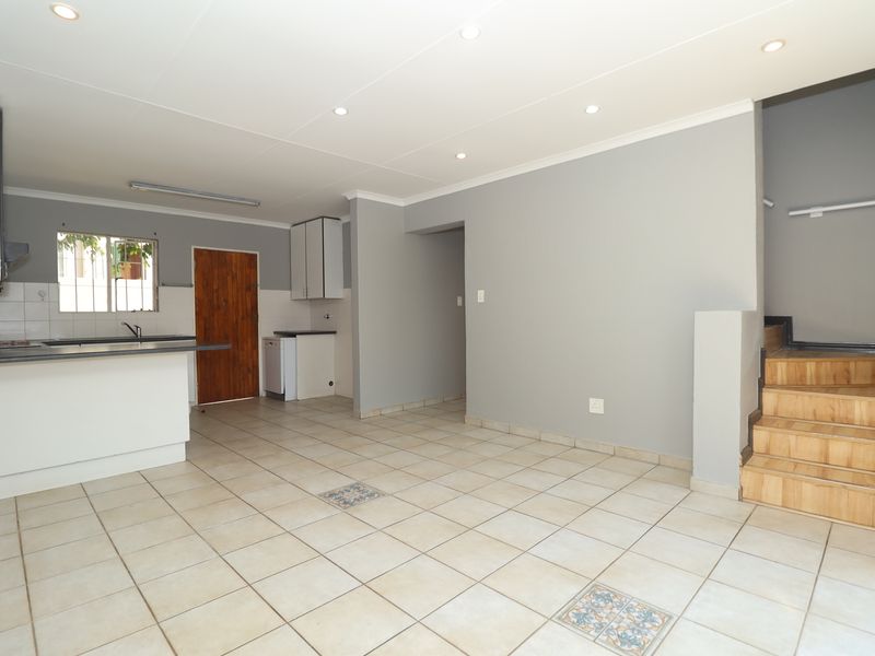 Open plan living area featuring a functional kitchen with cabinetry, tiled flooring throughout, and a wooden staircase leading to the upper level.
