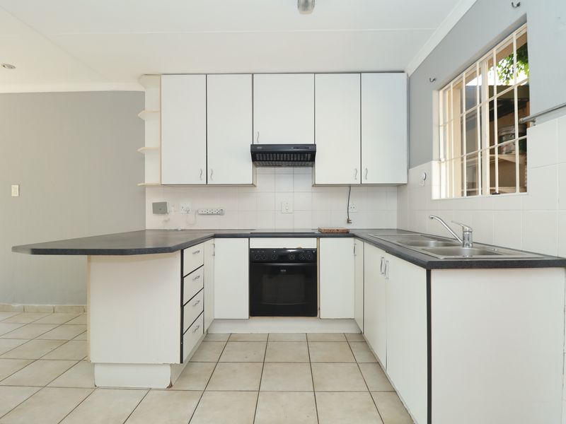 A functional kitchen featuring white cabinetry, laminate countertops, a built-in oven with extractor fan, and tiled flooring, offering a clean canvas for updates.