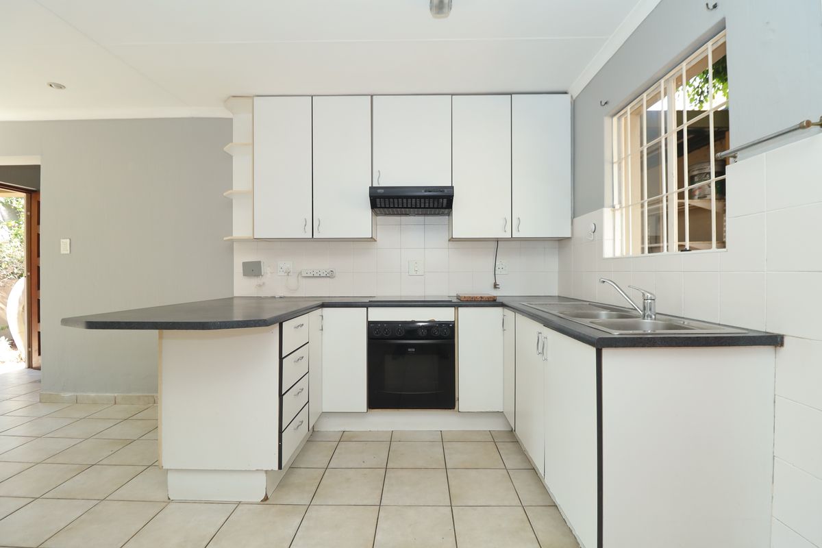 A functional kitchen featuring white cabinetry, laminate countertops, a built-in oven with extractor fan, and tiled flooring, offering a clean canvas for updates.