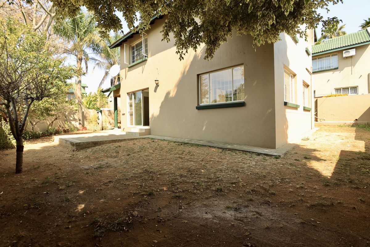 Rear view of the townhouse featuring a concrete patio, sliding glass doors, and a private garden area with established trees.