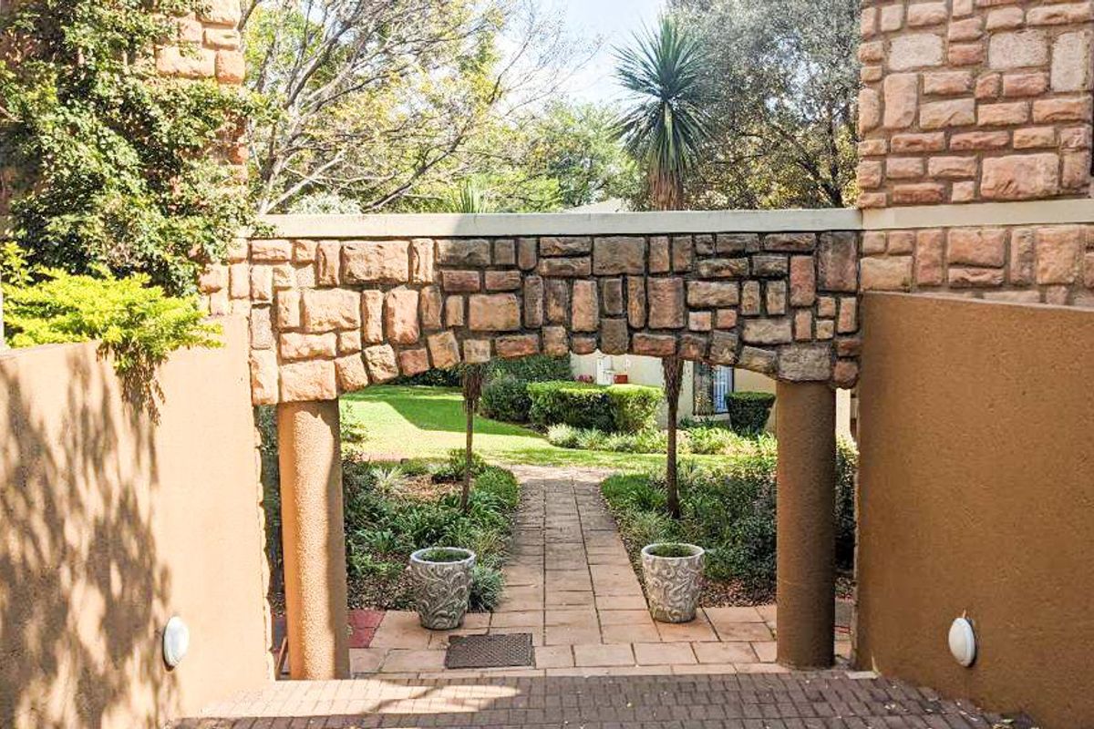 A view through a stone-clad archway leading to a paved garden path and landscaped outdoor area.