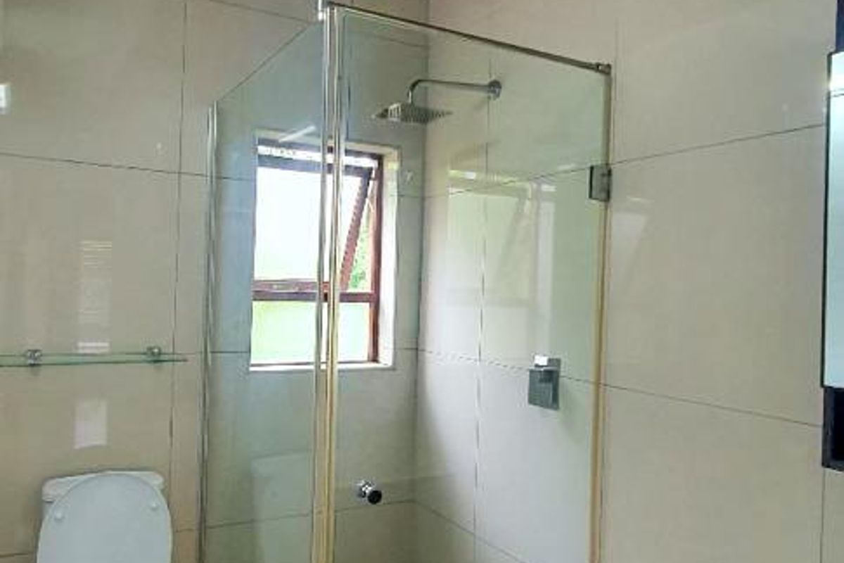 Modern bathroom featuring a glass-enclosed shower, tiled walls, and exposed wooden ceiling beams.