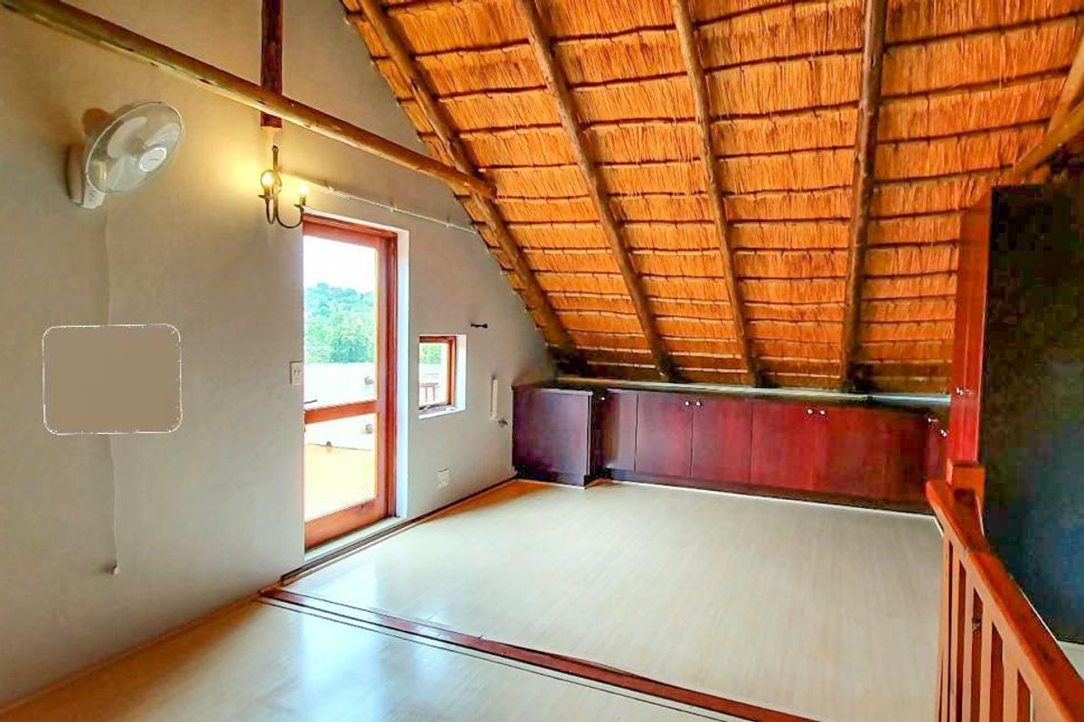 An attic-style bedroom featuring a vaulted thatched roof, built-in wooden cabinetry, laminate flooring, and access to a balcony through a glass door.