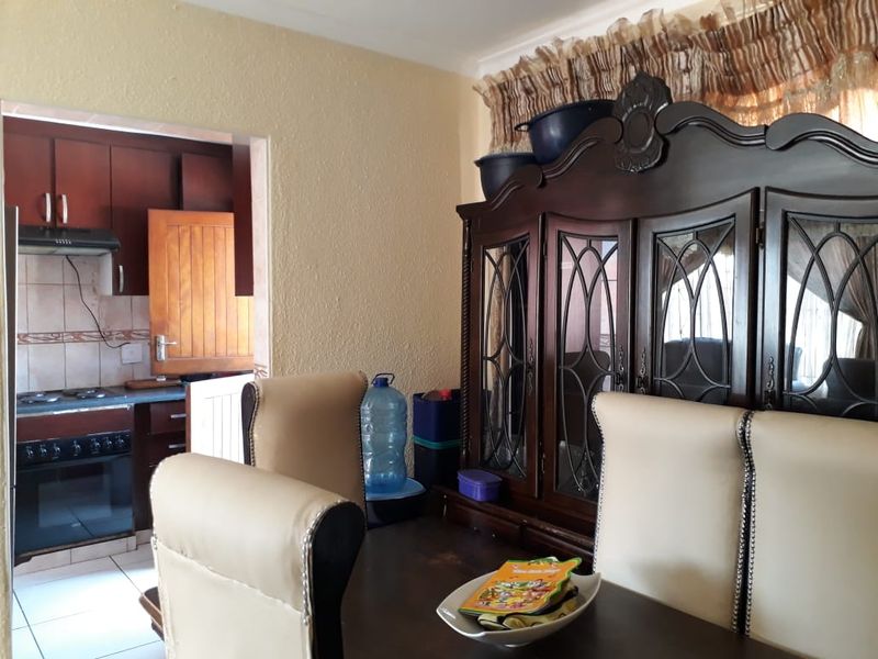 Open plan dining area adjacent to a functional kitchen featuring built-in cabinetry, oven, and hob with tiled flooring.