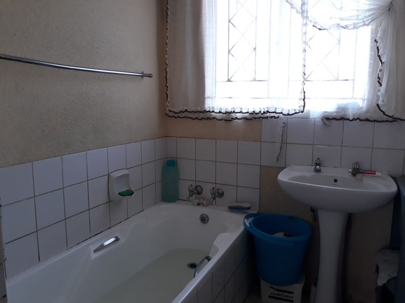A functional bathroom featuring a standard bathtub, pedestal basin, and tiled splashback, requiring cosmetic updates to modernize the space.