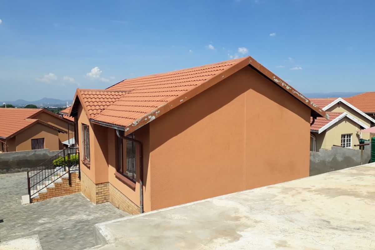 Rear view of a residential house featuring terracotta roof tiles, plastered walls, and a paved driveway area with some visible wear on fascia boards.