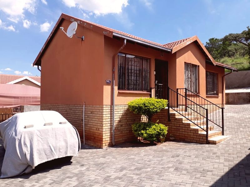 Front elevation of a single-story house featuring a brick base, tiled roof, paved driveway, and security bars on windows.