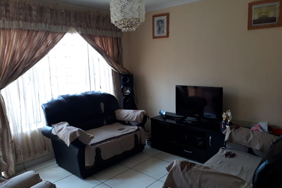 A living room featuring tiled flooring, a decorative ceiling light fixture, and a large window fitted with security bars.