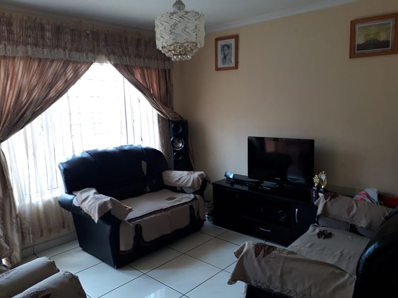 A living room featuring tiled flooring, a decorative ceiling light fixture, and a large window fitted with security bars.