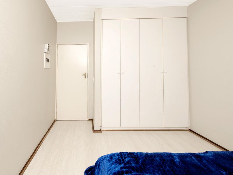 A bedroom featuring light-toned laminate flooring and white built-in cupboards, providing functional storage space within the room.