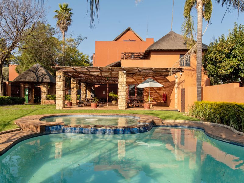 Outdoor pool area featuring a swimming pool, a covered patio with a timber pergola and stone pillars, and a thatched roof structure.