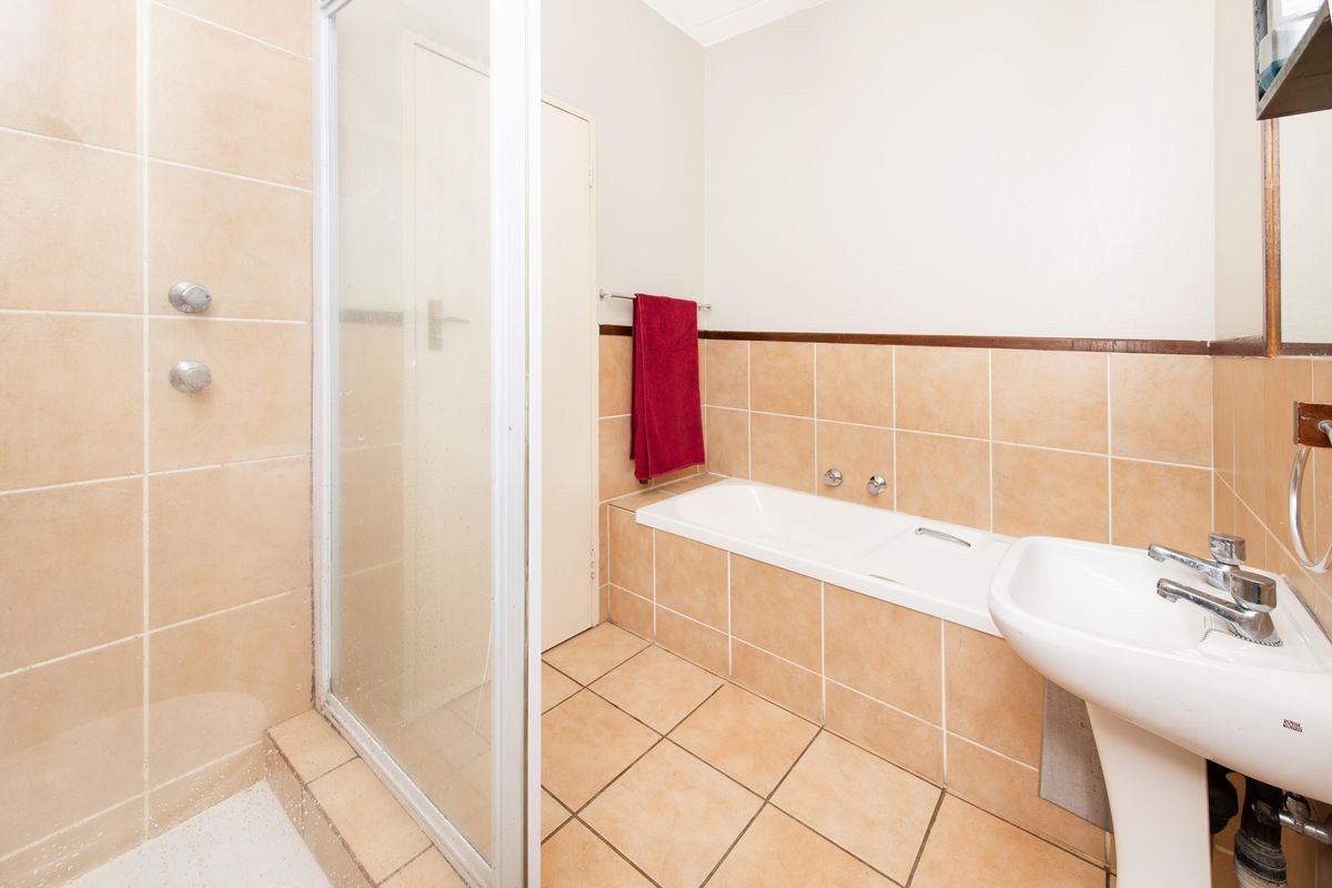 A functional bathroom featuring a separate shower enclosure, built-in bathtub, and pedestal washbasin with neutral ceramic tiling throughout.