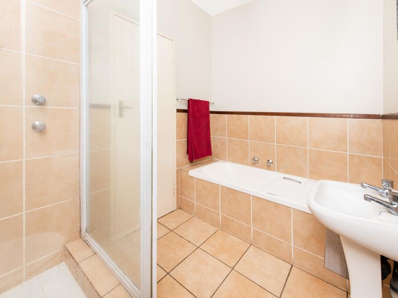 A functional bathroom featuring a separate shower enclosure, built-in bathtub, and pedestal washbasin with neutral ceramic tiling throughout.