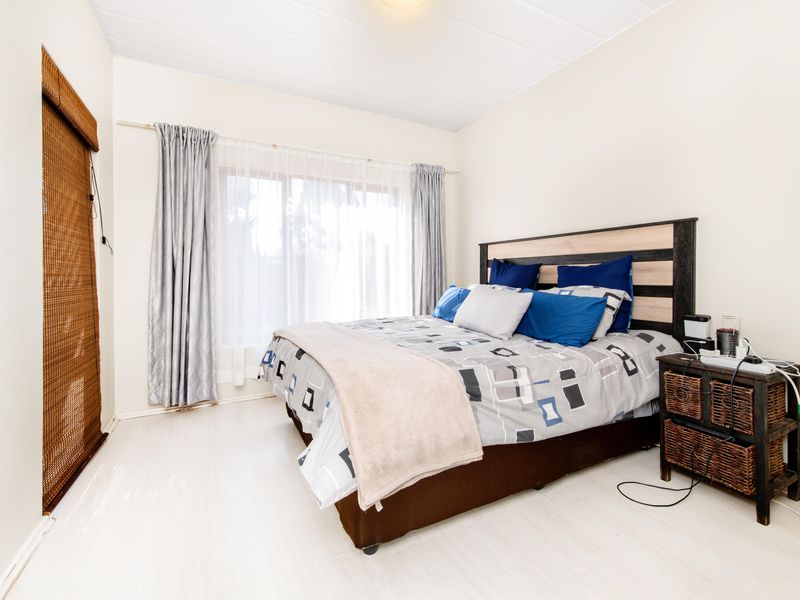 A bright bedroom featuring light-toned laminate flooring, a sliding door with blinds, and neutral wall finishes.