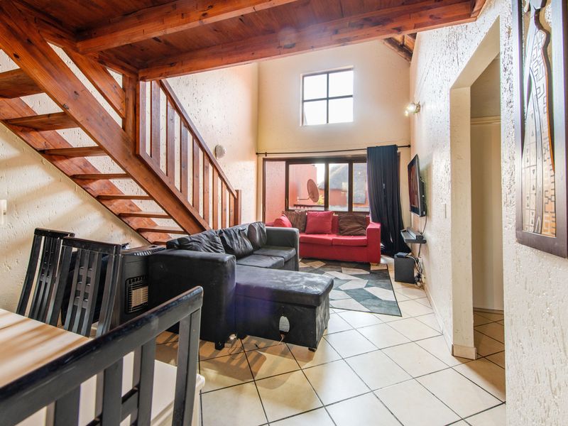Spacious living area featuring high ceilings with exposed timber beams, a wooden staircase, and tiled flooring, offering a bright and open atmosphere.