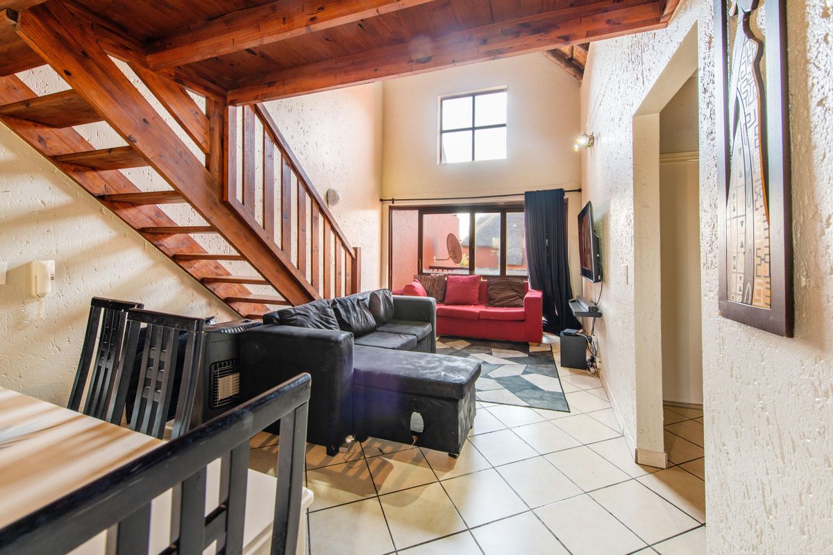Spacious living area featuring high ceilings with exposed timber beams, a wooden staircase, and tiled flooring, offering a bright and open atmosphere.