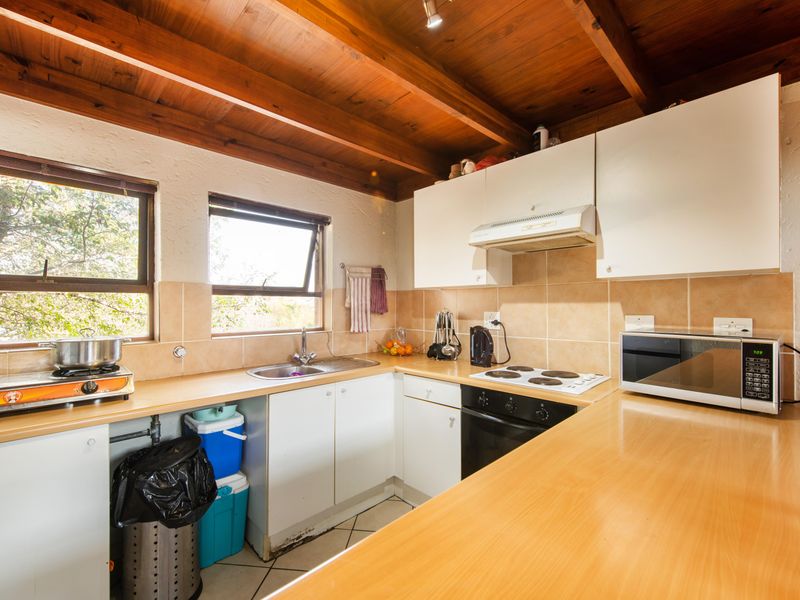 A functional kitchen featuring white cabinetry, laminate countertops, a tiled backsplash, and a distinctive exposed timber beam ceiling with natural light.