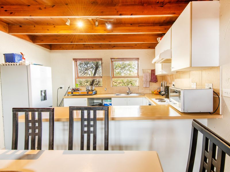 A functional kitchen featuring exposed timber ceiling beams, laminate countertops, a tiled backsplash, and built-in cabinetry with an integrated extractor fan.