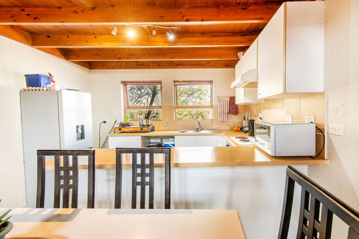 A functional kitchen featuring exposed timber ceiling beams, laminate countertops, a tiled backsplash, and built-in cabinetry with an integrated extractor fan.