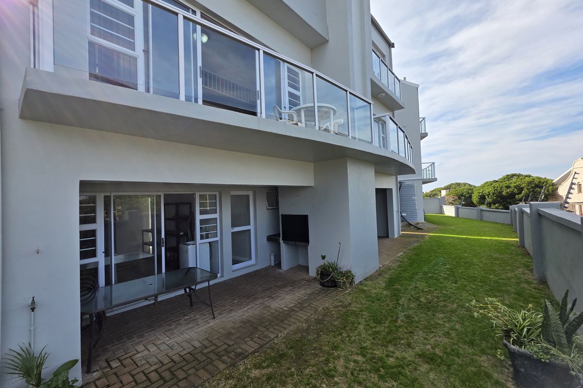 Rear view of the townhouse featuring a paved patio area, glass-balustraded balcony above, and a private garden space with boundary walling.