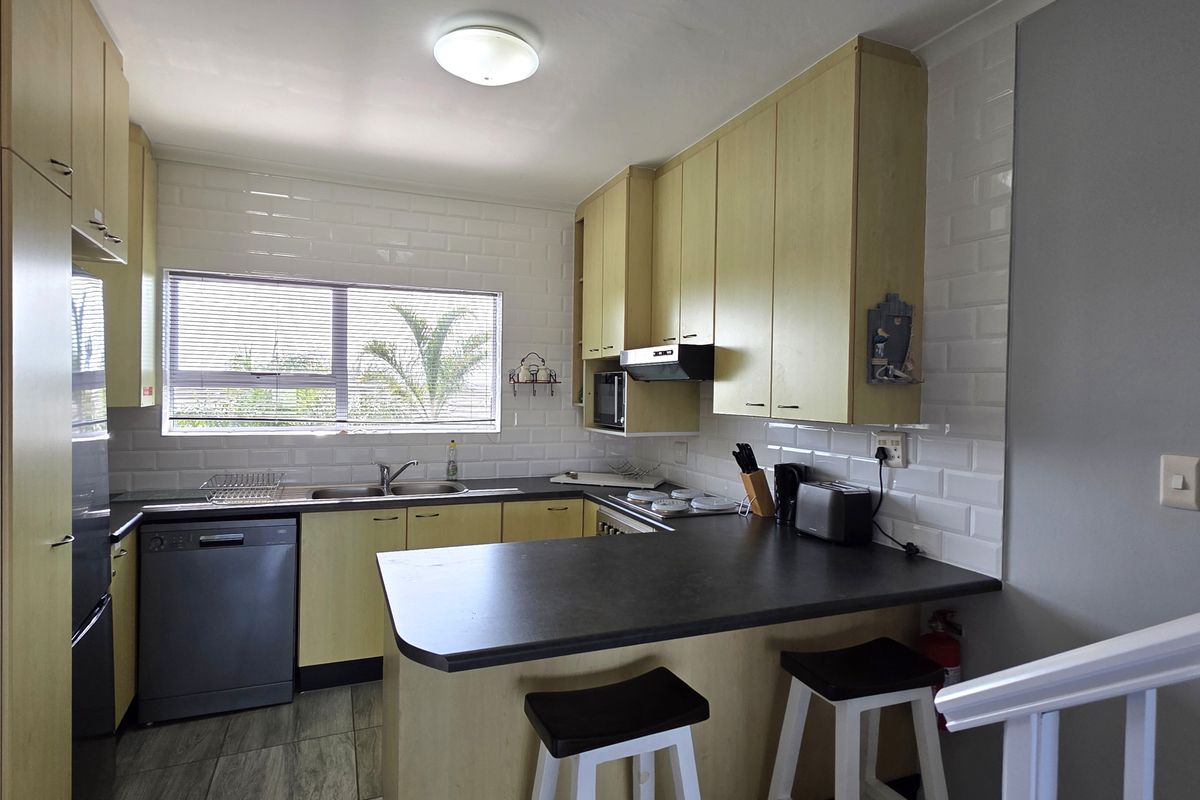 Functional kitchen featuring light wood-tone cabinetry, subway tile backsplash, dark laminate countertops, and integrated appliances with a breakfast bar area.