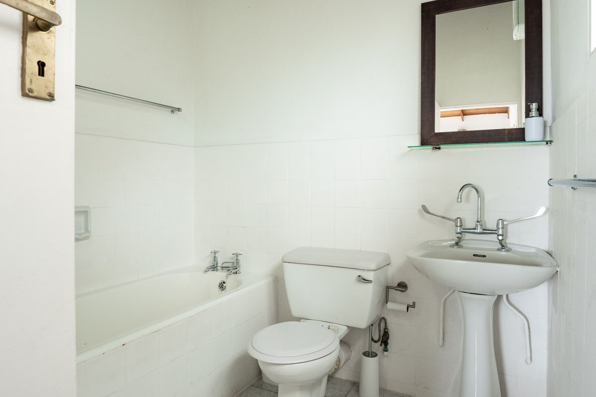 A functional bathroom featuring a white bathtub, pedestal basin, and toilet with classic chrome fixtures and wall-mounted mirror.