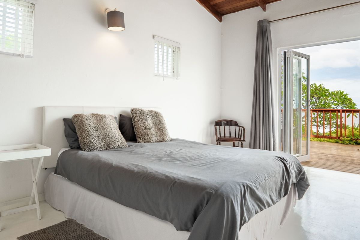 Bright bedroom featuring exposed timber ceiling beams and bi-fold doors opening onto a private wooden deck with scenic views.