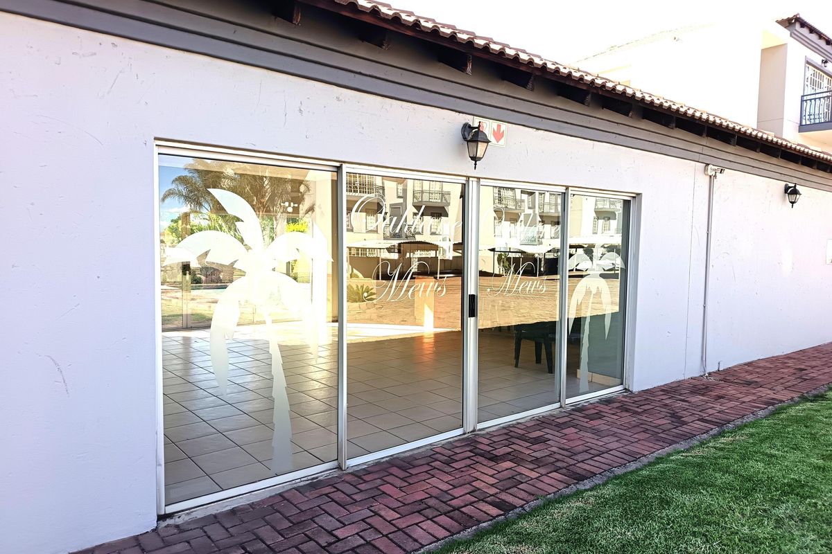 Exterior view of a ground floor apartment featuring large sliding glass doors, tiled flooring, and a brick paved walkway leading to the entrance.