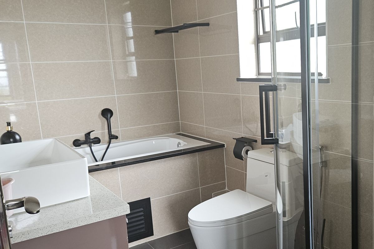 Modern bathroom featuring a built-in bathtub, glass-enclosed shower, toilet, and vanity basin with neutral wall and floor tiling.
