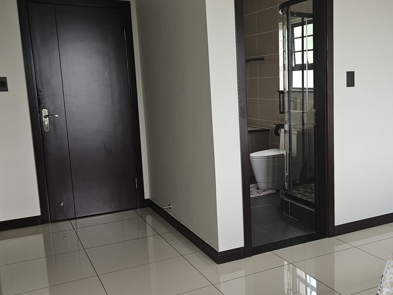 A clean, modern bedroom featuring neutral tiled flooring, dark wood-finish doors, and direct access to an en-suite bathroom.