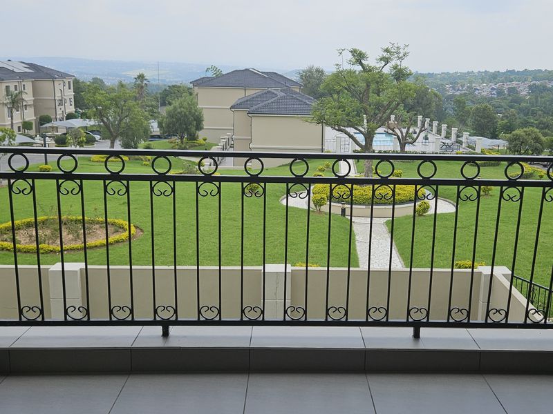 A spacious balcony featuring a decorative wrought iron balustrade and tiled flooring, offering elevated views over the complex gardens and surrounding landscape.
