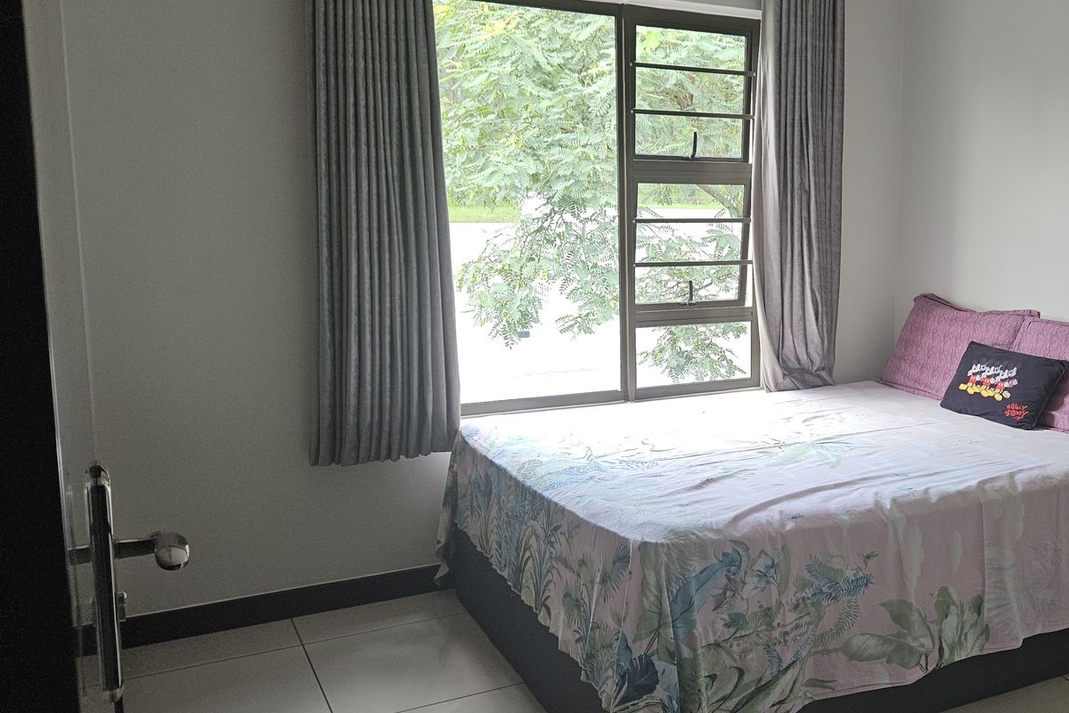 A well-maintained bedroom featuring neutral tiled flooring, clean wall finishes, and a large window with integrated security bars.