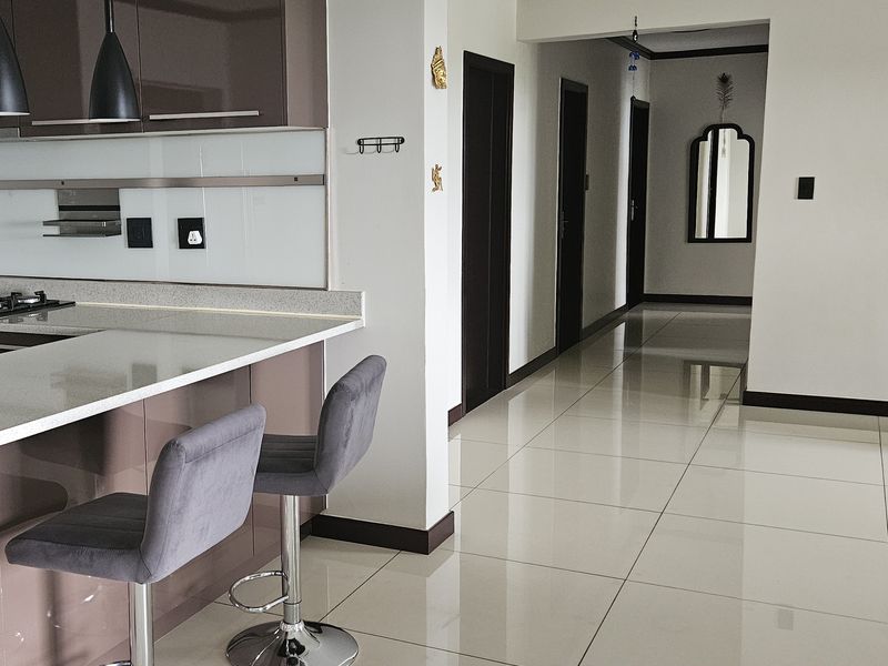 Modern open-plan kitchen featuring high-gloss cabinetry, stone countertops, and a gas hob, seamlessly flowing into a tiled hallway with clean architectural lines.