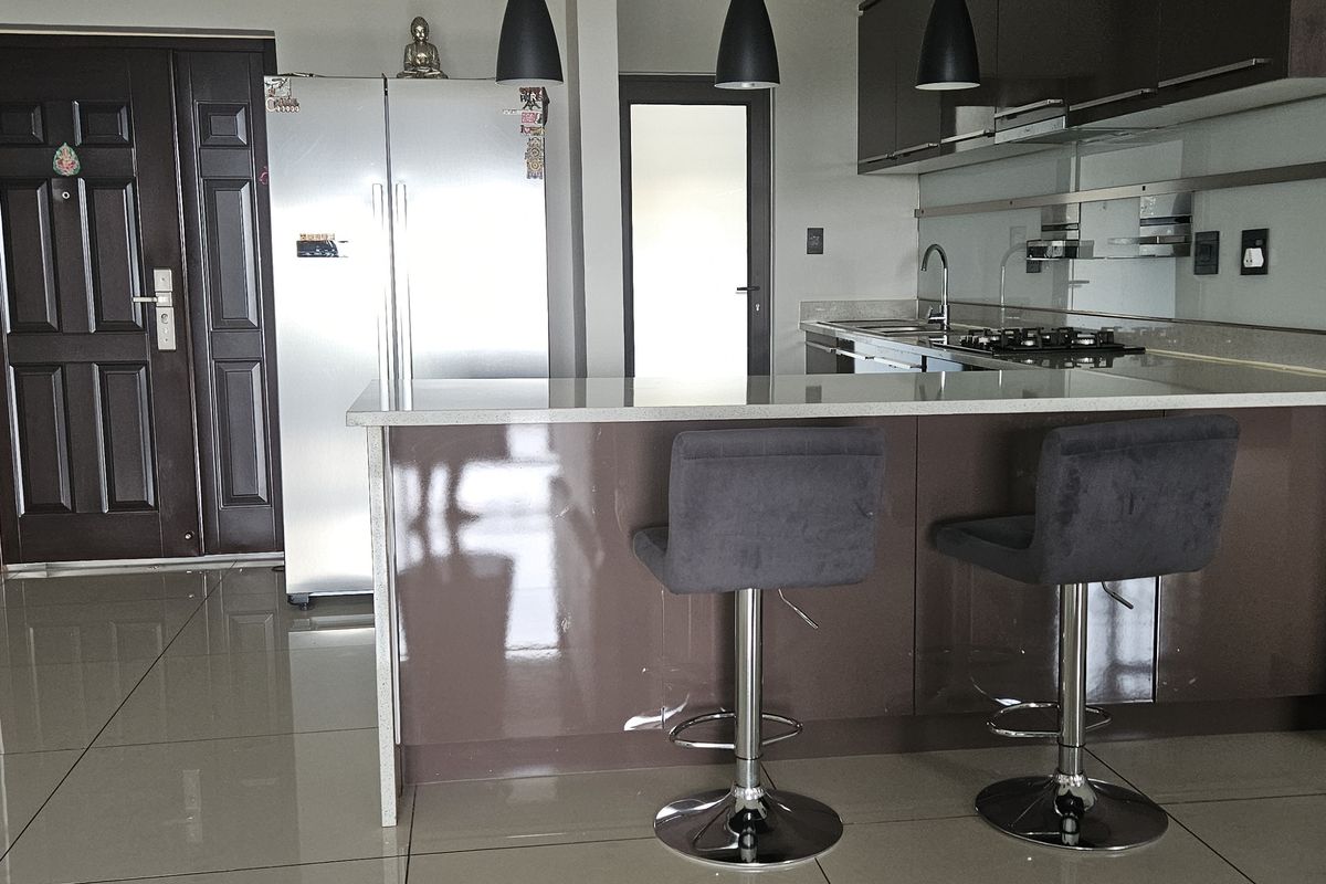 Modern kitchen featuring a central island with stone countertops, sleek cabinetry, gas hob, and contemporary pendant lighting, finished with polished floor tiles.