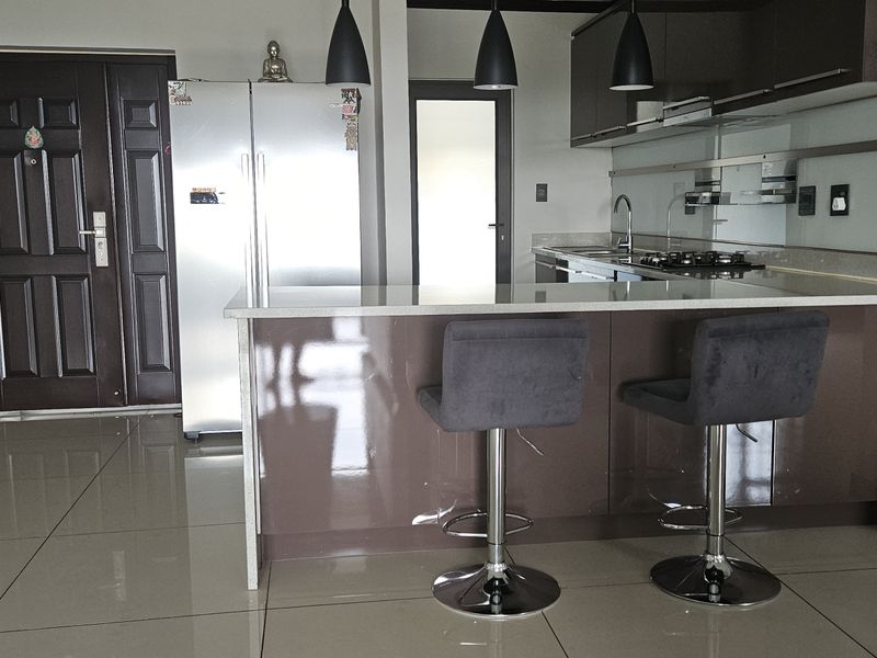Modern kitchen featuring a central island with stone countertops, sleek cabinetry, gas hob, and contemporary pendant lighting, finished with polished floor tiles.