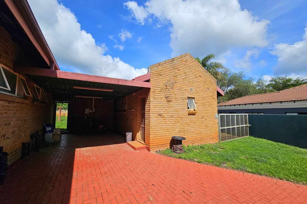Rear exterior view featuring a face brick facade, covered carport area, and red brick paved driveway leading to a small lawn.
