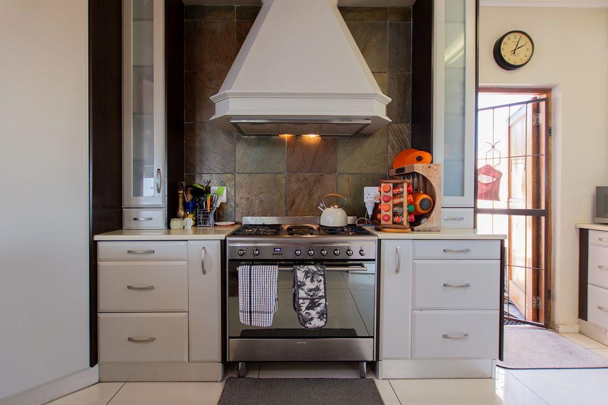 A well-maintained kitchen featuring a gas stove, extractor fan, stone tile backsplash, and ample built-in cabinetry with stone countertops.