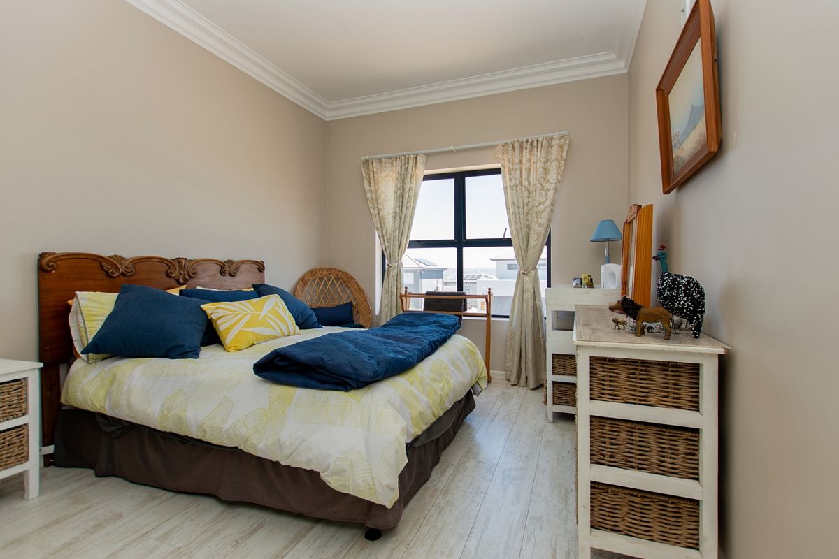 A well-maintained bedroom featuring light-toned laminate flooring, decorative ceiling cornicing, and a large aluminium-framed window providing natural light.