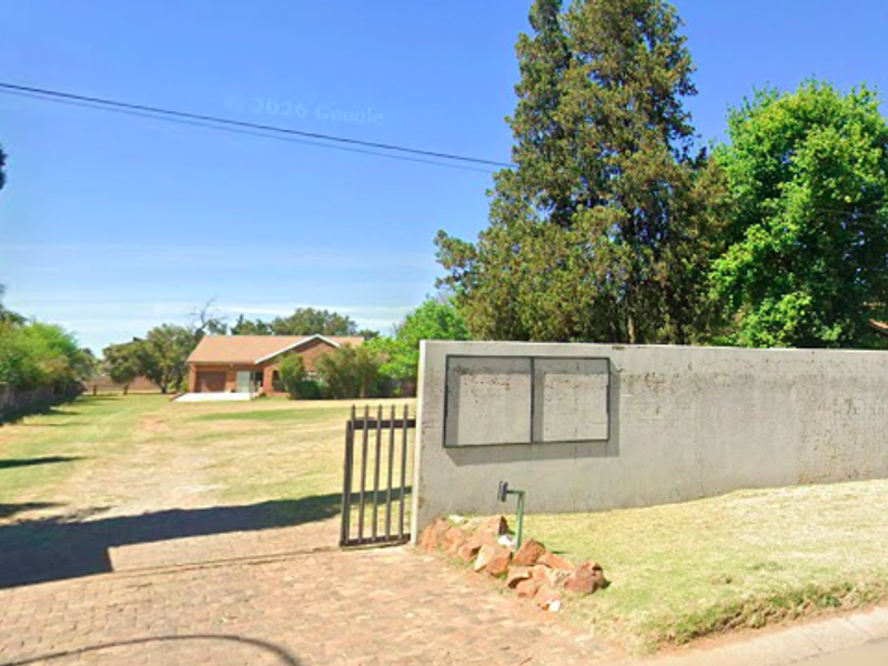 Street view of a residential vacant land property featuring a perimeter wall, gated entrance, and paved driveway leading to the site.