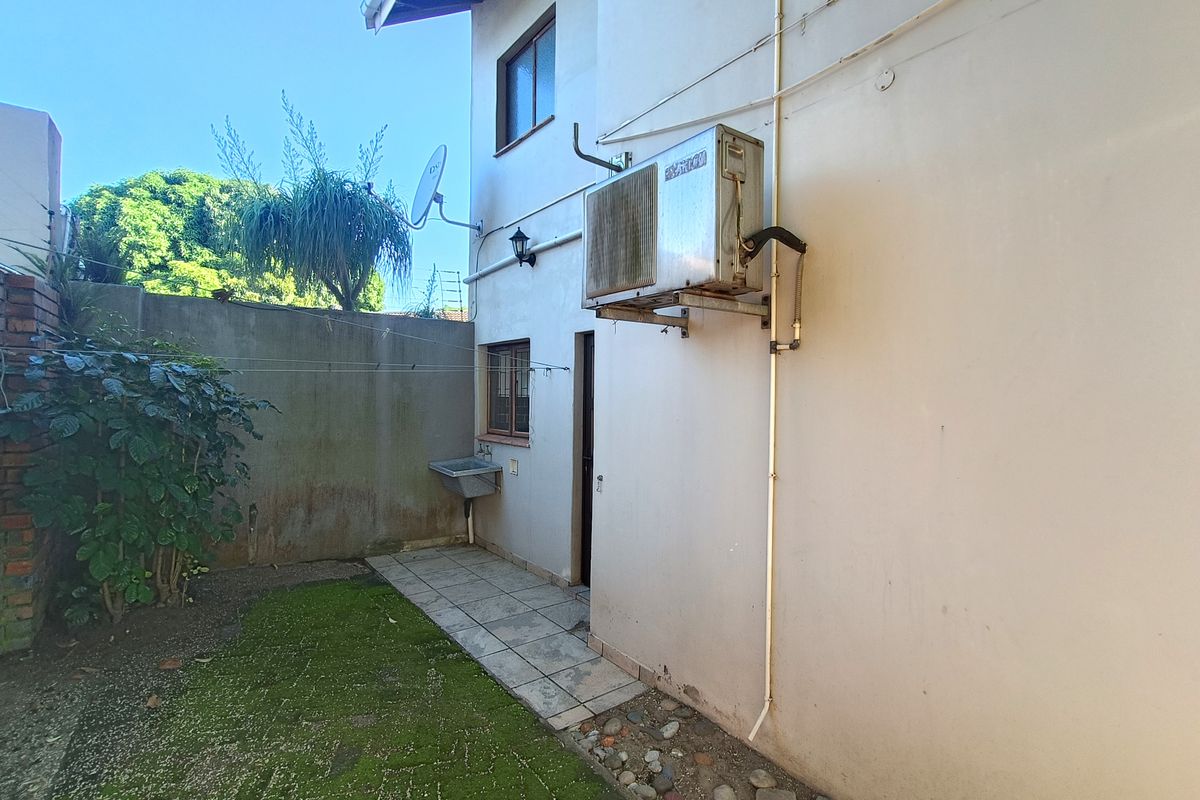 Rear exterior area featuring a utility sink, tiled walkway, and wall-mounted air conditioning unit, with a small garden space and boundary wall.