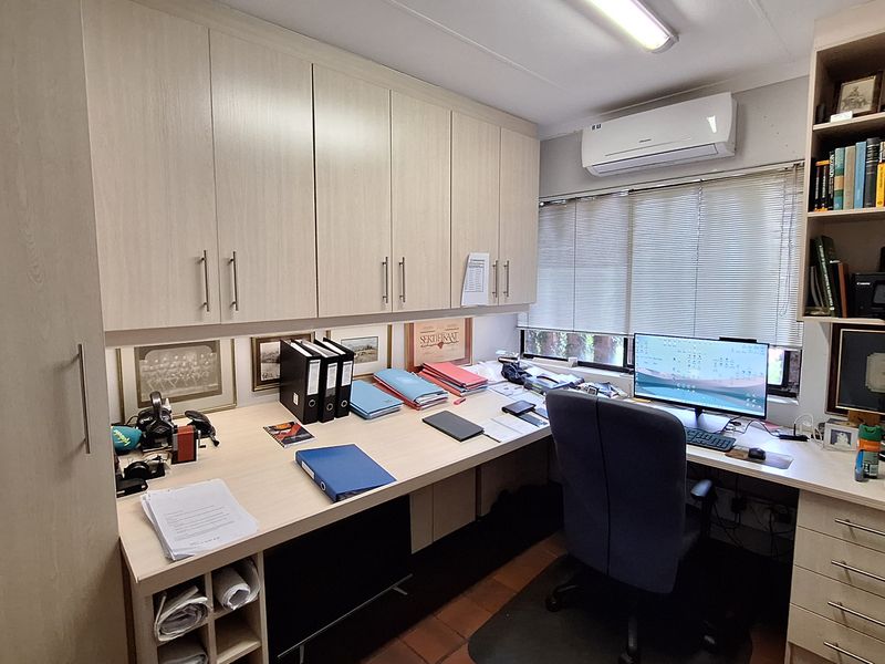 A functional home office featuring extensive built-in cabinetry, a spacious desk area, and a wall-mounted air conditioning unit.
