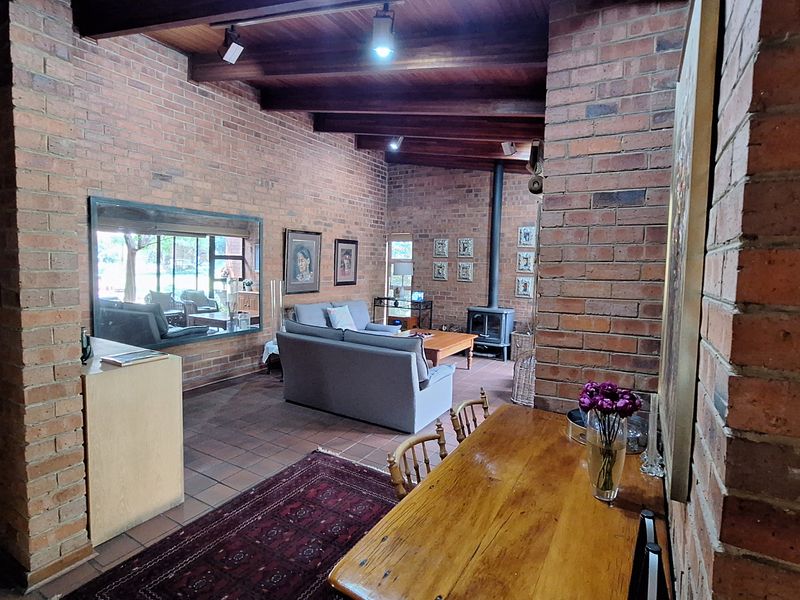 Spacious living area featuring exposed brick walls, high timber-beamed ceilings, tiled flooring, and a built-in wood-burning fireplace.