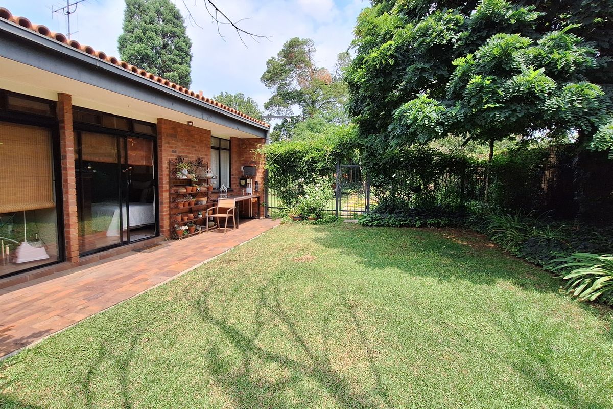 A private rear garden featuring a paved patio area, established lawn, and mature perimeter landscaping, accessible via sliding glass doors.