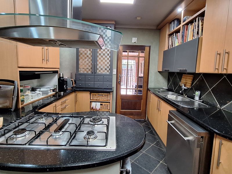 A functional kitchen featuring dark granite countertops, a gas hob with a glass extractor hood, integrated cabinetry, and slate flooring.