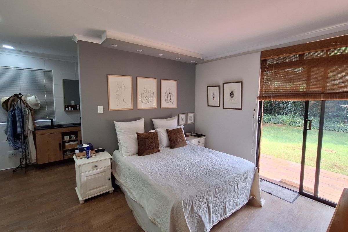 A well-maintained bedroom featuring a recessed ceiling light feature, sliding glass doors leading to a garden deck, and an integrated en-suite vanity area.